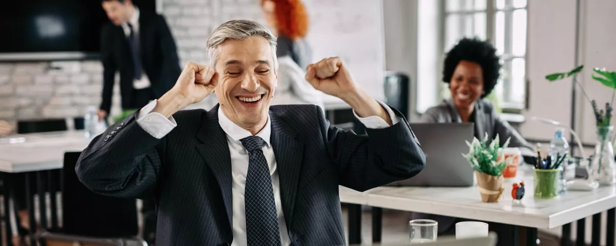 Homme d'affaires joyeux levant les poings en signe de victoire lors d'une réunion d'équipe au bureau.