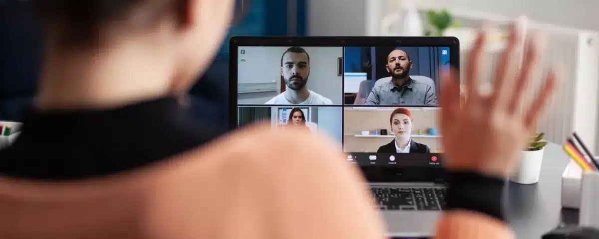 Manager en visioconférence faisant un signe de la main lors d'une réunion en anglais, illustrant la communication efficace en équipe hybride.