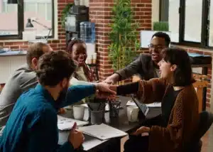 Équipe diversifiée unissant leurs mains au-dessus d'une table de réunion pour symboliser la collaboration et la réussite d'un projet.
