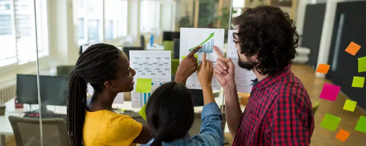 Une équipe collaborative analyse des indicateurs de performance clés (KPI) et des graphiques de croissance sur un mur de bureau, illustrant l'union entre hard skills et soft skills.