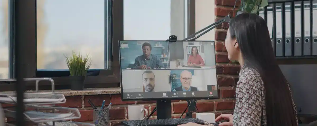 Femme en réunion sur Google Meet suivant une visioconférence à quatre participants sur son écran d'ordinateur de bureau.