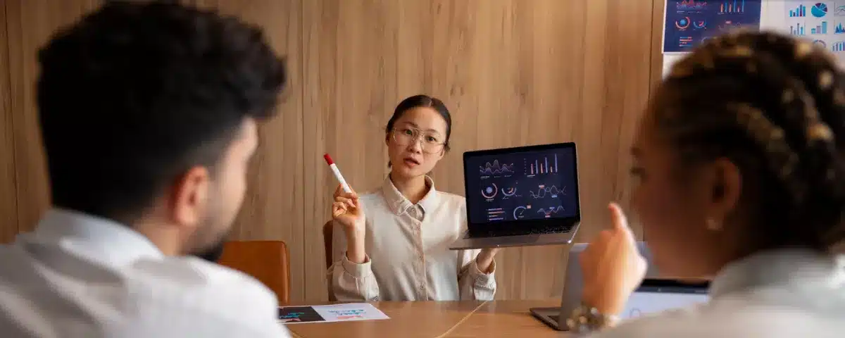 Une femme d'affaires présente un tableau de bord d'analyse de données sur un ordinateur portable lors d'une réunion d'équipe.