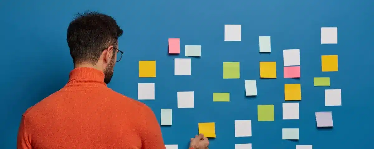 Manager de projet de dos planifiant un workflow sur un mur bleu avec des post-it multicolores.