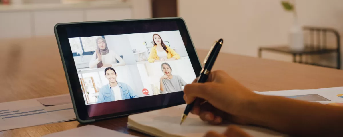 Utilisateur participant à une réunion en ligne sur tablette et écrivant un compte-rendu professionnel.