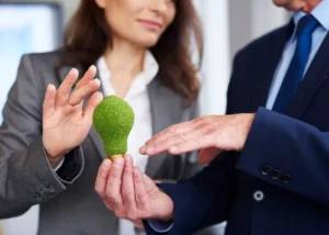 Professionnels en entreprise tenant une ampoule recouverte de mousse verte, illustrant le cadre juridique des allégations environnementales et de la conformité écoresponsable.