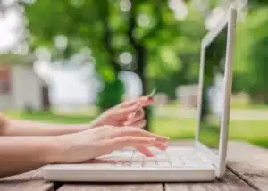 Personne travaillant sur un ordinateur portable en extérieur dans un cadre verdoyant, illustrant la sobriété numérique et les bonnes pratiques écoresponsables au quotidien.
