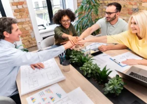 Équipe de collaborateurs souriants réunie autour d'une table de réunion avec les mains empilées au centre, illustrant l'impact de la QVCT et du bien-être sur la santé mentale au travail.